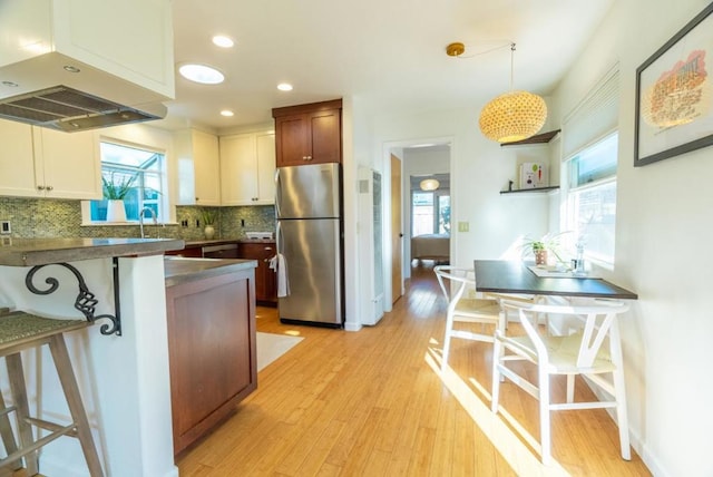 kitchen featuring pendant lighting, stainless steel fridge, a kitchen breakfast bar, island range hood, and white cabinets