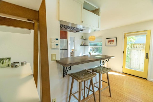 kitchen with stainless steel refrigerator, white cabinetry, a healthy amount of sunlight, and light hardwood / wood-style flooring