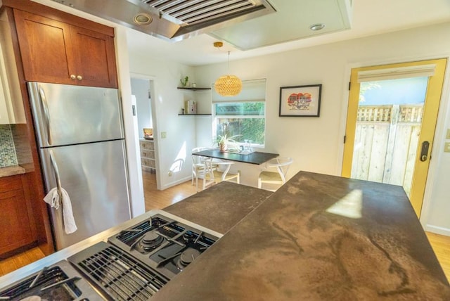 kitchen featuring stove, decorative light fixtures, stainless steel fridge, and light wood-type flooring