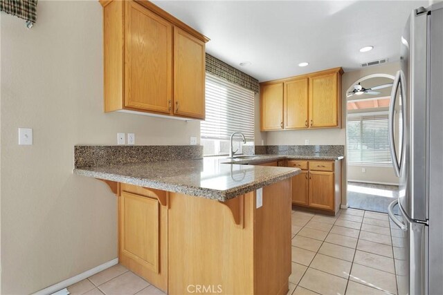 kitchen featuring light tile patterned flooring, sink, stainless steel refrigerator, kitchen peninsula, and light stone countertops