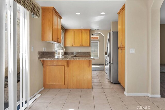 kitchen with sink, light tile patterned floors, stainless steel fridge, and kitchen peninsula