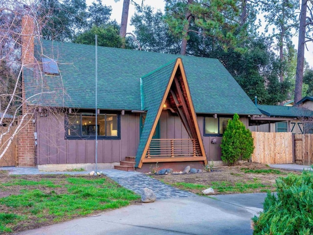 a-frame style home with a shingled roof, board and batten siding, and fence