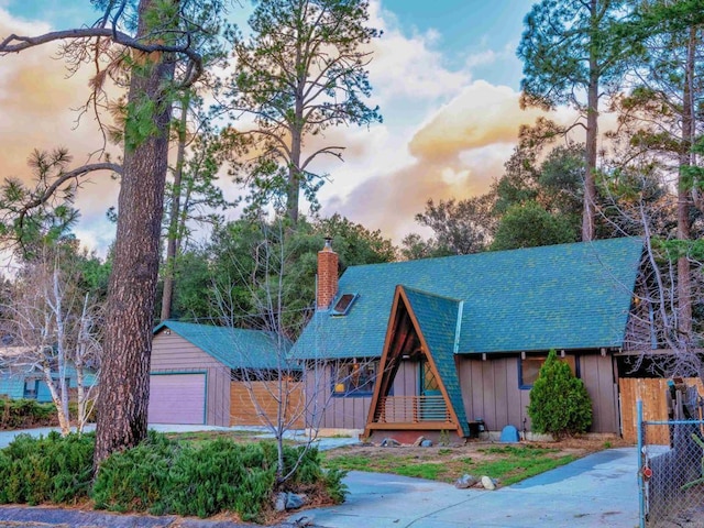 a-frame style home with a detached garage, a chimney, an outbuilding, fence, and board and batten siding