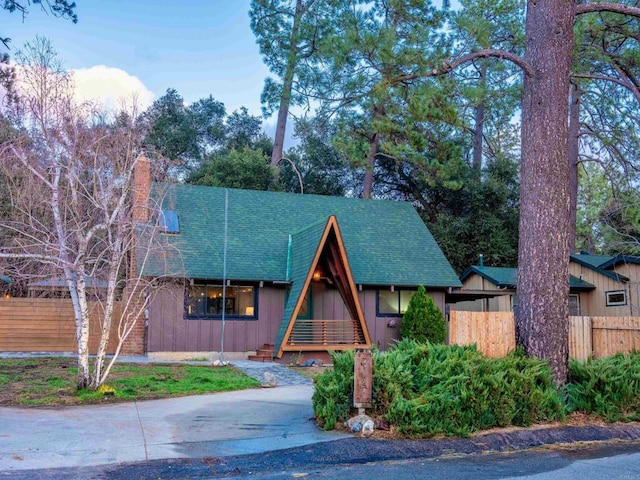 a-frame style home with board and batten siding, a chimney, roof with shingles, and fence