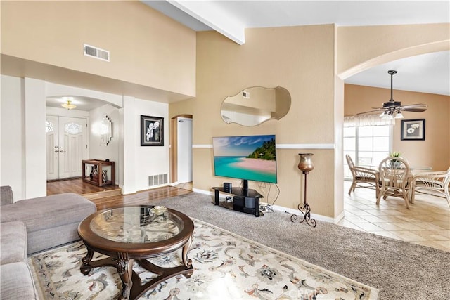 living room with ceiling fan, light colored carpet, beam ceiling, and high vaulted ceiling