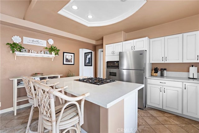 kitchen with a breakfast bar area, appliances with stainless steel finishes, white cabinetry, a kitchen island, and a raised ceiling