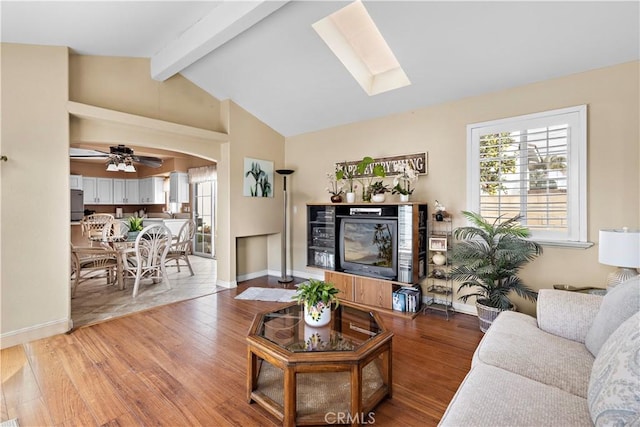 living room with ceiling fan, hardwood / wood-style flooring, and vaulted ceiling with skylight