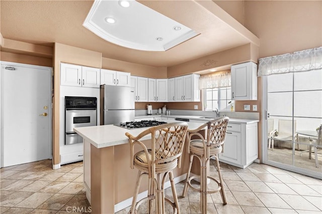 kitchen with appliances with stainless steel finishes, white cabinetry, a breakfast bar area, a center island, and a tray ceiling