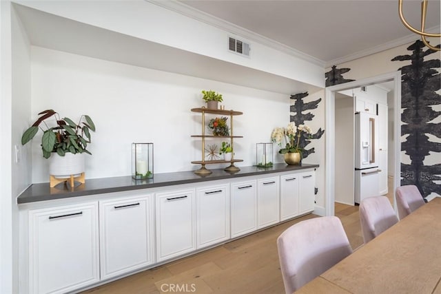 bar with crown molding, high end white fridge, light wood-style floors, and visible vents