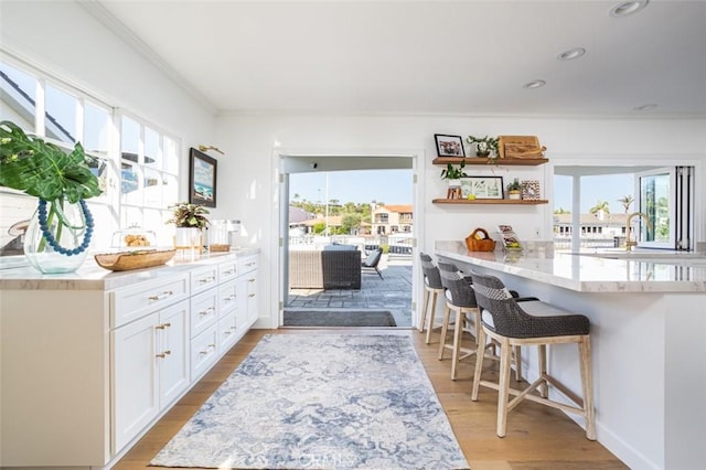 kitchen with a kitchen breakfast bar, open shelves, light wood-style floors, white cabinetry, and a sink