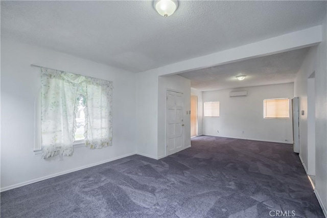 spare room featuring dark carpet, a wall unit AC, and a textured ceiling