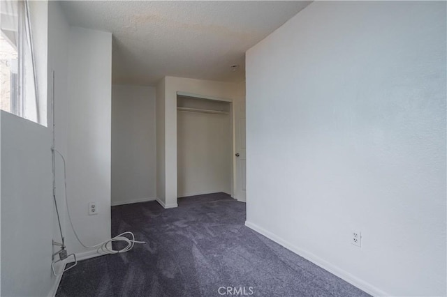 unfurnished bedroom with a textured ceiling, a closet, and dark colored carpet