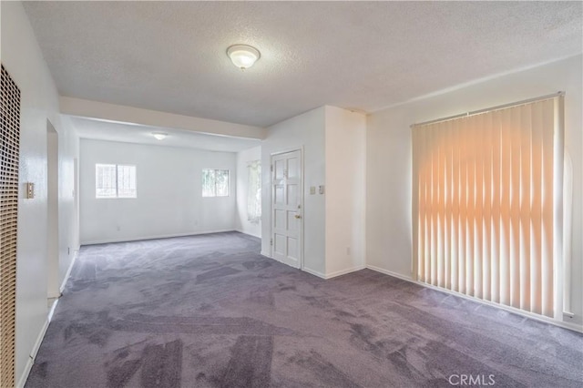 unfurnished room featuring a textured ceiling and dark carpet