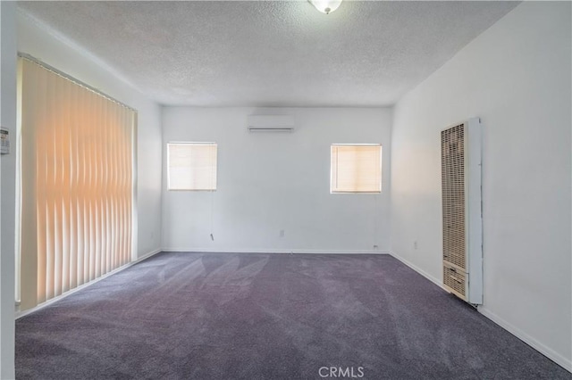 carpeted empty room featuring a wall mounted AC, a textured ceiling, and a wealth of natural light