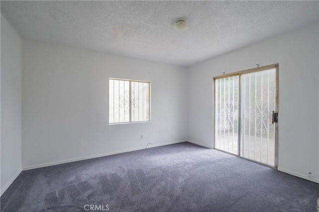 spare room featuring dark carpet and a textured ceiling