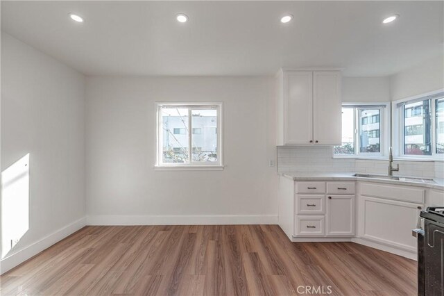 kitchen featuring sink, range, white cabinetry, decorative backsplash, and light wood-type flooring