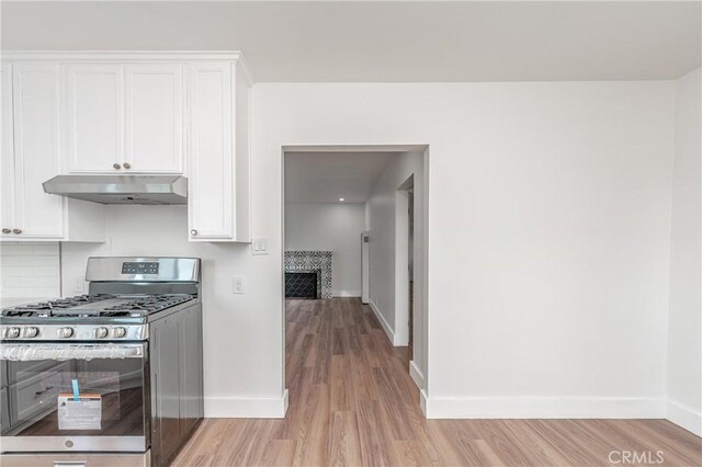 kitchen featuring white cabinetry, backsplash, stainless steel gas range oven, and light hardwood / wood-style floors