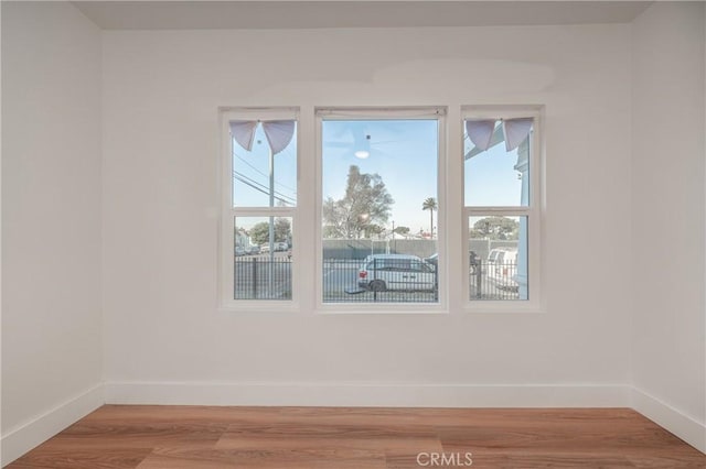 empty room with light wood finished floors, a wealth of natural light, and baseboards