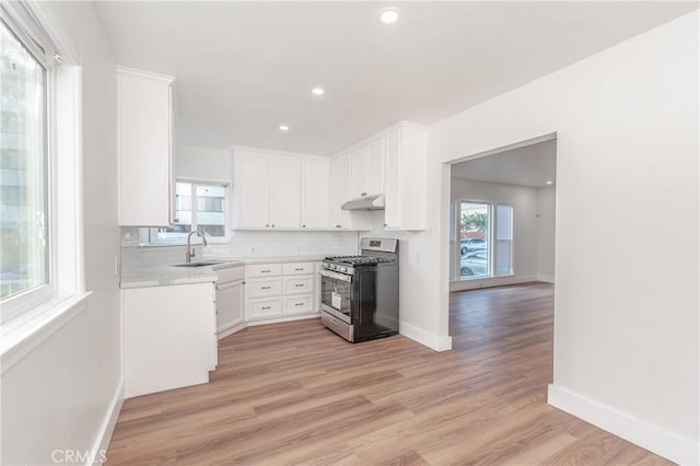 kitchen featuring light wood finished floors, backsplash, a sink, stainless steel gas range, and under cabinet range hood