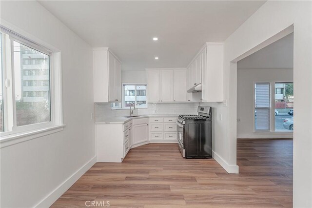 kitchen with sink, stainless steel gas range oven, white cabinetry, light hardwood / wood-style floors, and decorative backsplash