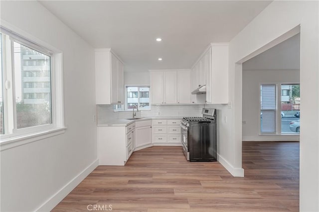 kitchen with a sink, white cabinetry, backsplash, and stainless steel range with gas stovetop