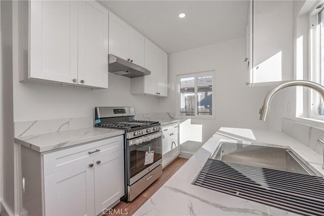 kitchen with sink, white cabinetry, light stone countertops, gas stove, and light wood-type flooring