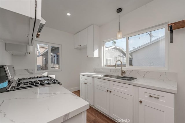 kitchen featuring light stone countertops, gas range, white cabinetry, and a sink