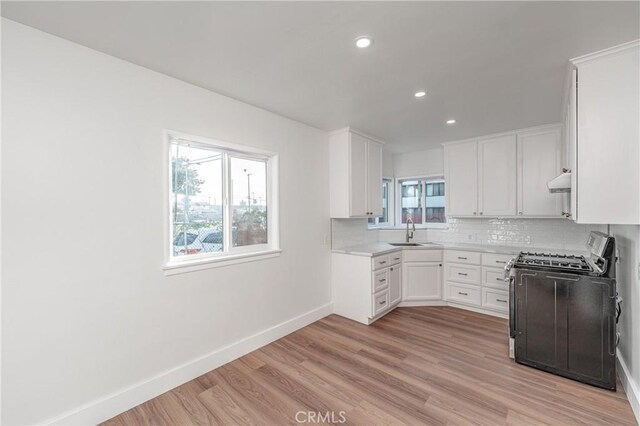 kitchen with sink, gas stove, tasteful backsplash, light hardwood / wood-style floors, and white cabinets