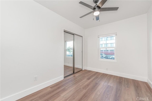 unfurnished bedroom with light wood-style flooring, baseboards, ceiling fan, and a closet