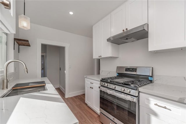 kitchen featuring white cabinets, light stone counters, under cabinet range hood, stainless steel range with gas cooktop, and a sink