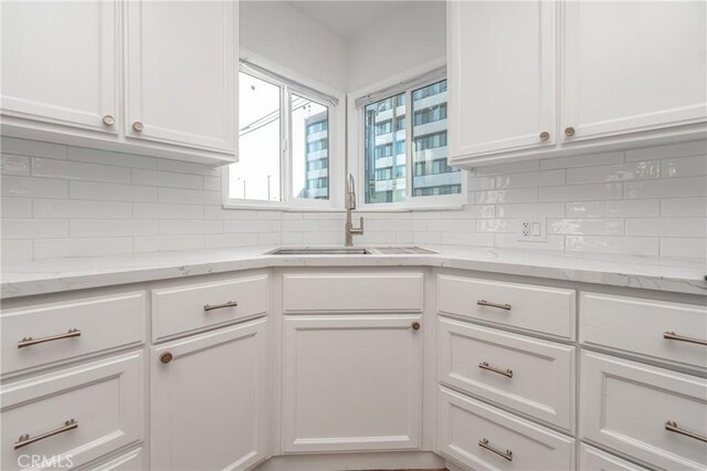 kitchen with white cabinetry, light stone countertops, and sink