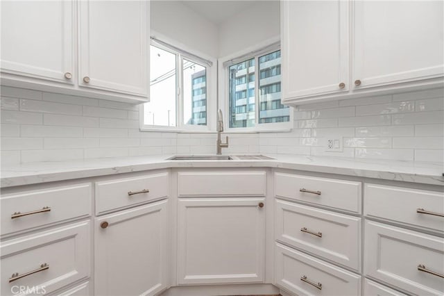 kitchen with light stone counters, white cabinets, a sink, and decorative backsplash