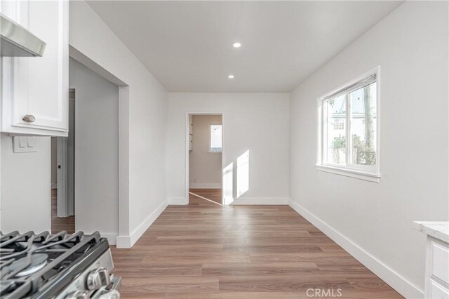 interior space featuring white cabinetry, stainless steel range with gas stovetop, exhaust hood, and light wood-type flooring