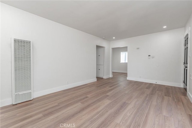 unfurnished room with light wood finished floors, a heating unit, recessed lighting, and baseboards