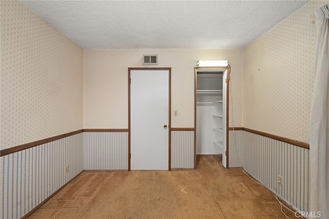 unfurnished bedroom with a closet, carpet flooring, a textured ceiling, and a spacious closet