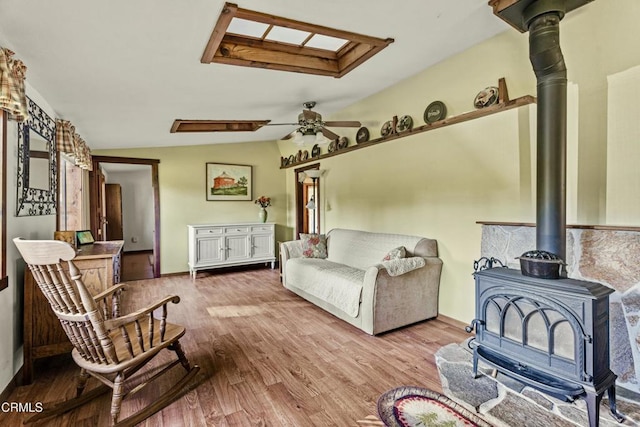 living room with ceiling fan, lofted ceiling, a wood stove, and light hardwood / wood-style floors