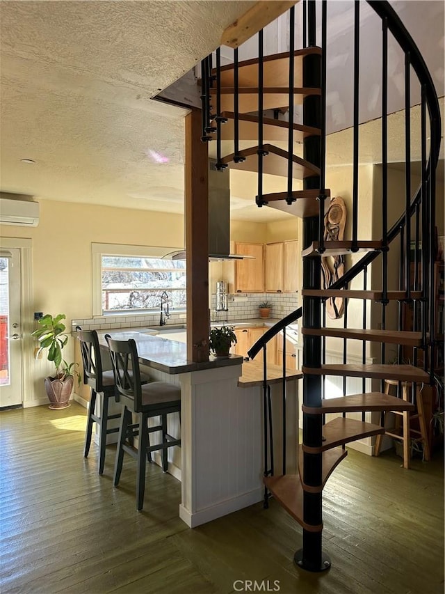 interior space with dark hardwood / wood-style floors, light brown cabinetry, decorative backsplash, and an AC wall unit