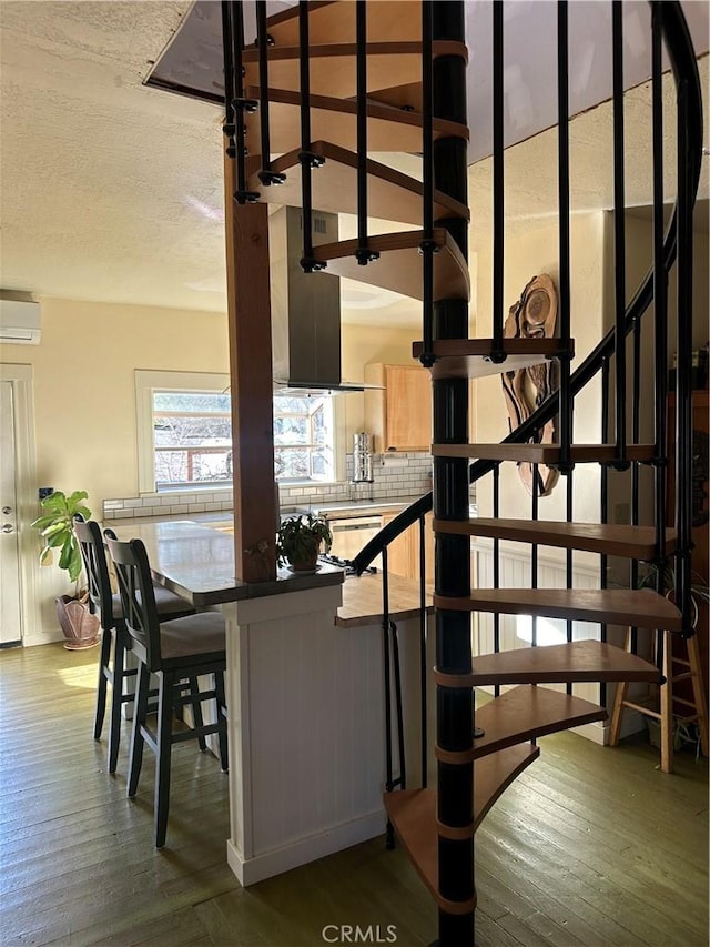 stairs with hardwood / wood-style flooring, an AC wall unit, and a textured ceiling