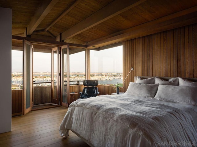 bedroom featuring beam ceiling, wood walls, wood ceiling, light hardwood / wood-style flooring, and access to exterior