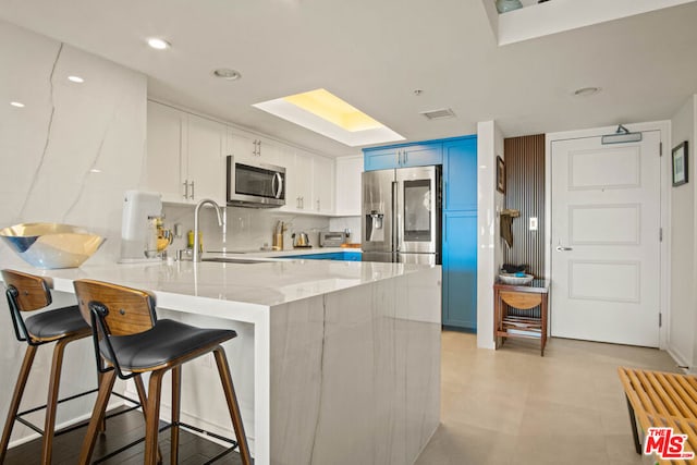 kitchen featuring blue cabinetry, white cabinetry, kitchen peninsula, stainless steel appliances, and backsplash