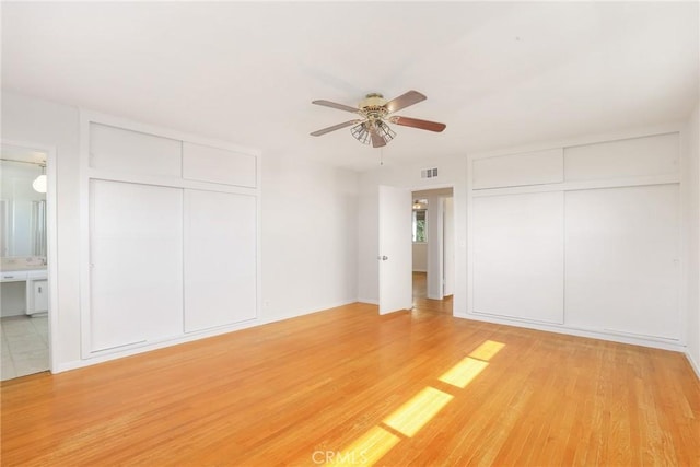 unfurnished bedroom with ceiling fan, connected bathroom, light hardwood / wood-style floors, and two closets