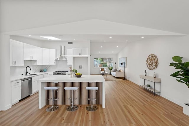 kitchen featuring wall chimney range hood, stainless steel dishwasher, white cabinets, and a kitchen island