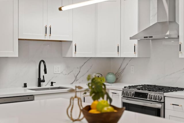 kitchen with wall chimney exhaust hood, stainless steel gas range, sink, white cabinetry, and decorative backsplash