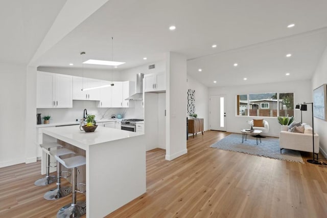 kitchen featuring wall chimney exhaust hood, a kitchen bar, stainless steel gas range oven, a center island, and white cabinets