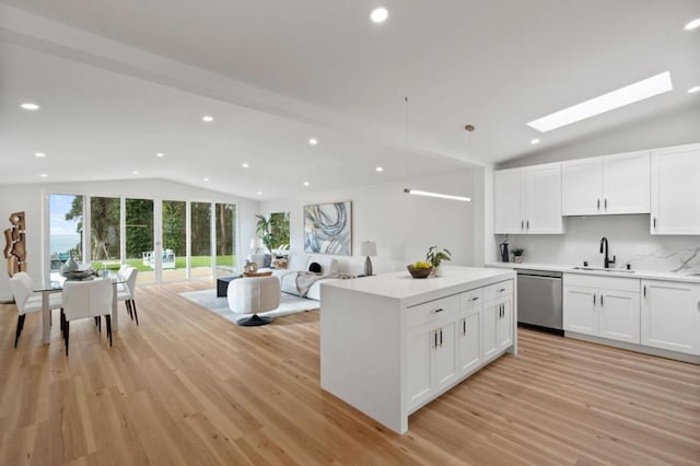 kitchen featuring vaulted ceiling with skylight, white cabinetry, sink, hanging light fixtures, and stainless steel dishwasher