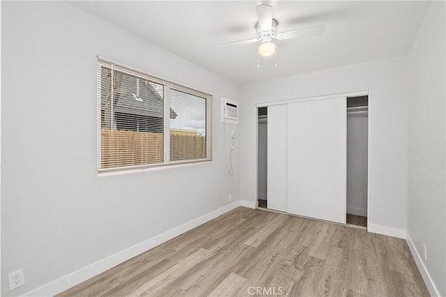 unfurnished bedroom featuring ceiling fan, a wall mounted air conditioner, light wood-type flooring, and a closet