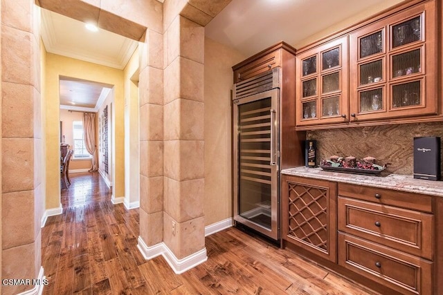 bar featuring light stone counters, crown molding, dark hardwood / wood-style flooring, and beverage cooler