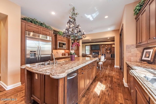 kitchen featuring built in appliances, decorative light fixtures, dark hardwood / wood-style floors, a kitchen island with sink, and decorative backsplash