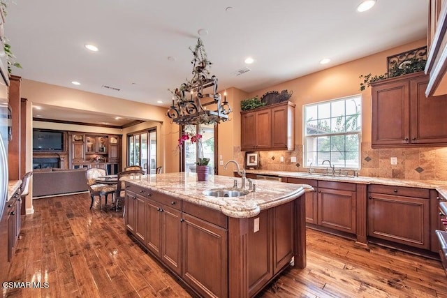 kitchen featuring sink, decorative backsplash, wood-type flooring, and an island with sink