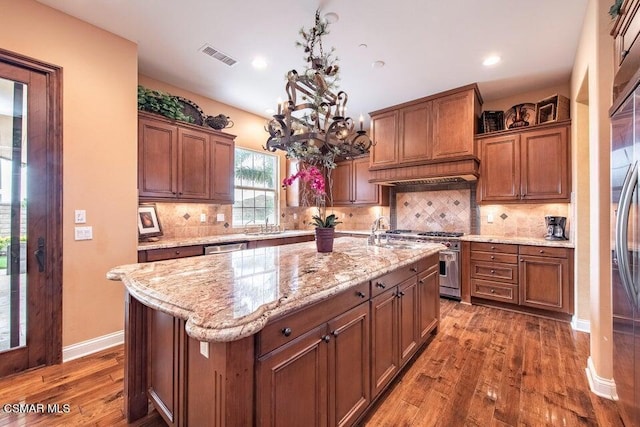 kitchen with decorative light fixtures, dark wood-type flooring, stainless steel appliances, and an island with sink